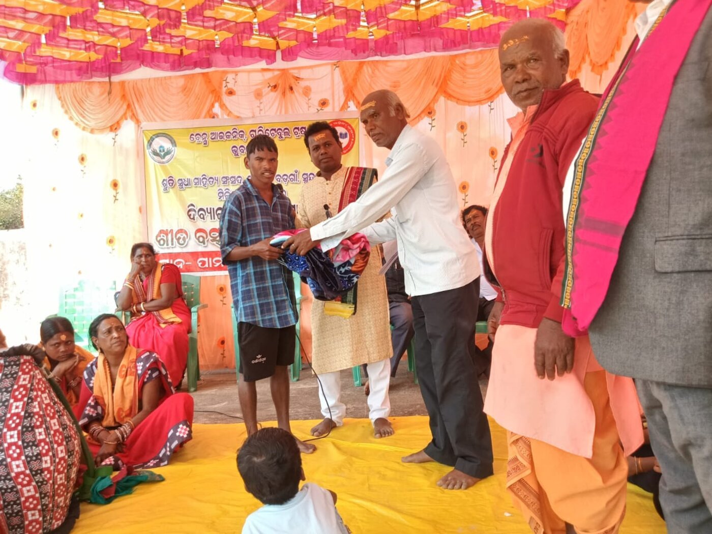 A Brains Iconic Charitable Trust volunteer hands warm winter clothing to a young resident during a distribution ceremony in Odisha.