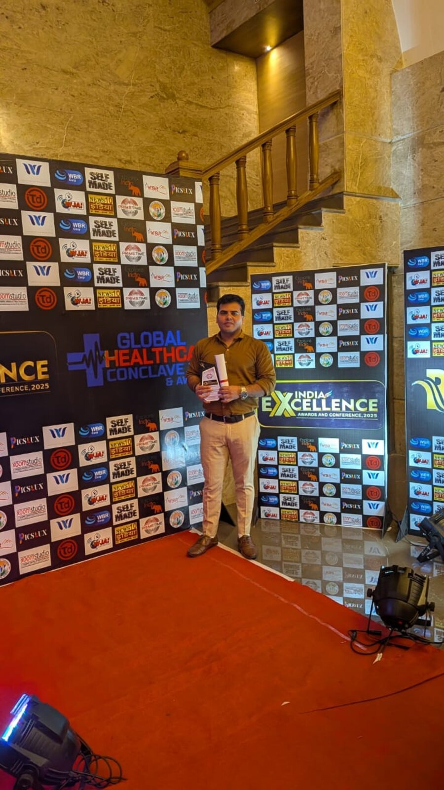 A Brains Iconic Charitable Trust representative on stage at the Global Healthcare Conclave and Awards 2025, holding the India Excellence Award trophy.